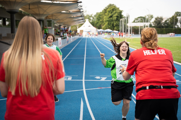Man sieht zwei Special Olympics-Athletinnen die ins Ziel zu ihren Helferinnen laufen.