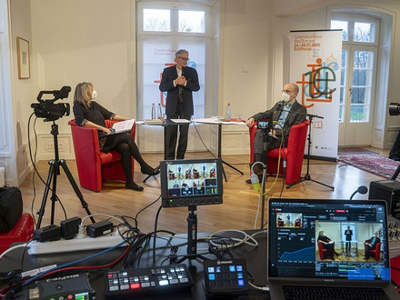 Das Bild zeigt zwei Menschen mit Corona-Schutzmasken in Sesseln im Literaturhaus aus der Anfangszeit. Im Vordergrund ist viel Videotechnik zu sehen, damals wurden Autorenlesungen nur online angeboten.