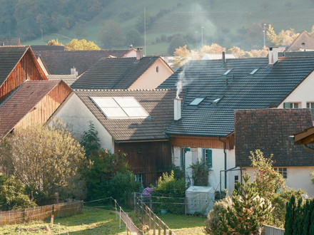Auf dem Foto sind mehrere Einfamilienhäuser im Frühjahr zu sehen. Der Schornstein eines Hauses raucht.