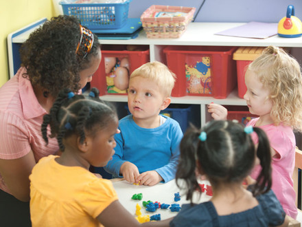 Vier Kindergartenkinder mit einer Erzieherin im Kindergarten