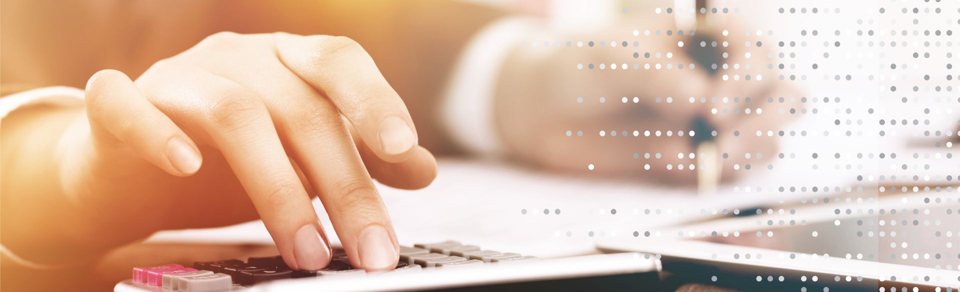 Man sieht die Hände einer Person, die auf einem Taschenrechner tippen und auf einem Tablet schreiben